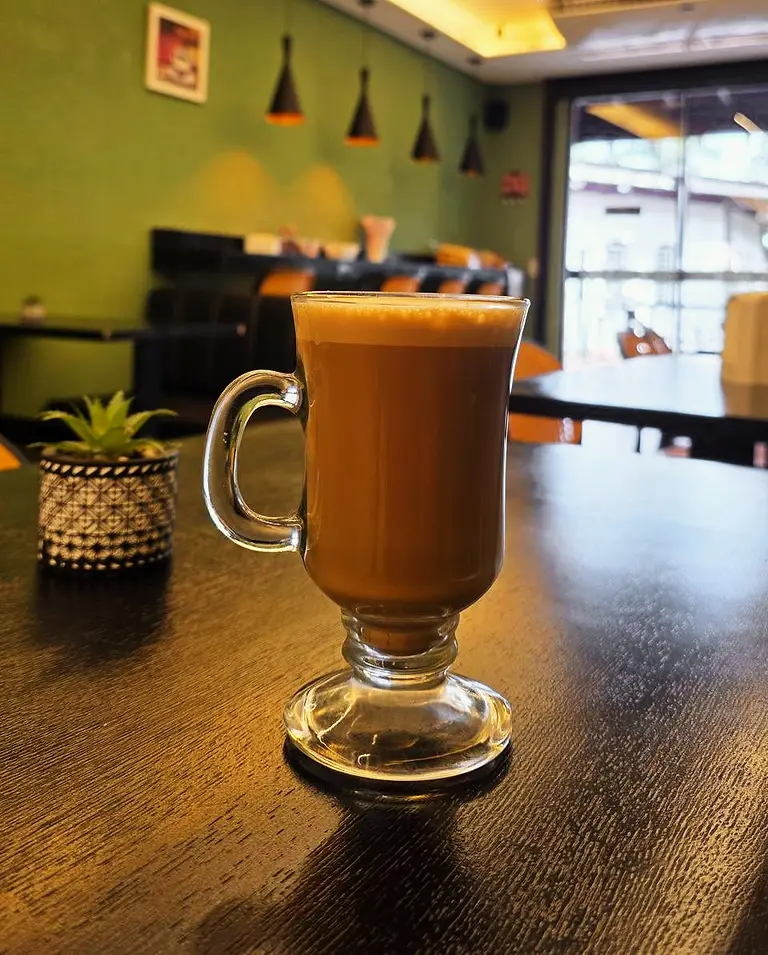 Café com leite em taça de vidro sobre a mesa preta do salão