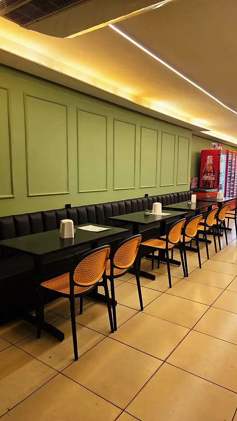 Salão com parede verde de boiserie, sofás pretos e cadeiras de palhinha